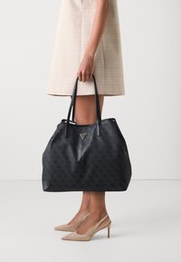 Zwarte leren tote bag met een gestructureerd patroon, dubbele handvatten en een zilveren logo-accent. Heeft een ruime en zachte silhouet.