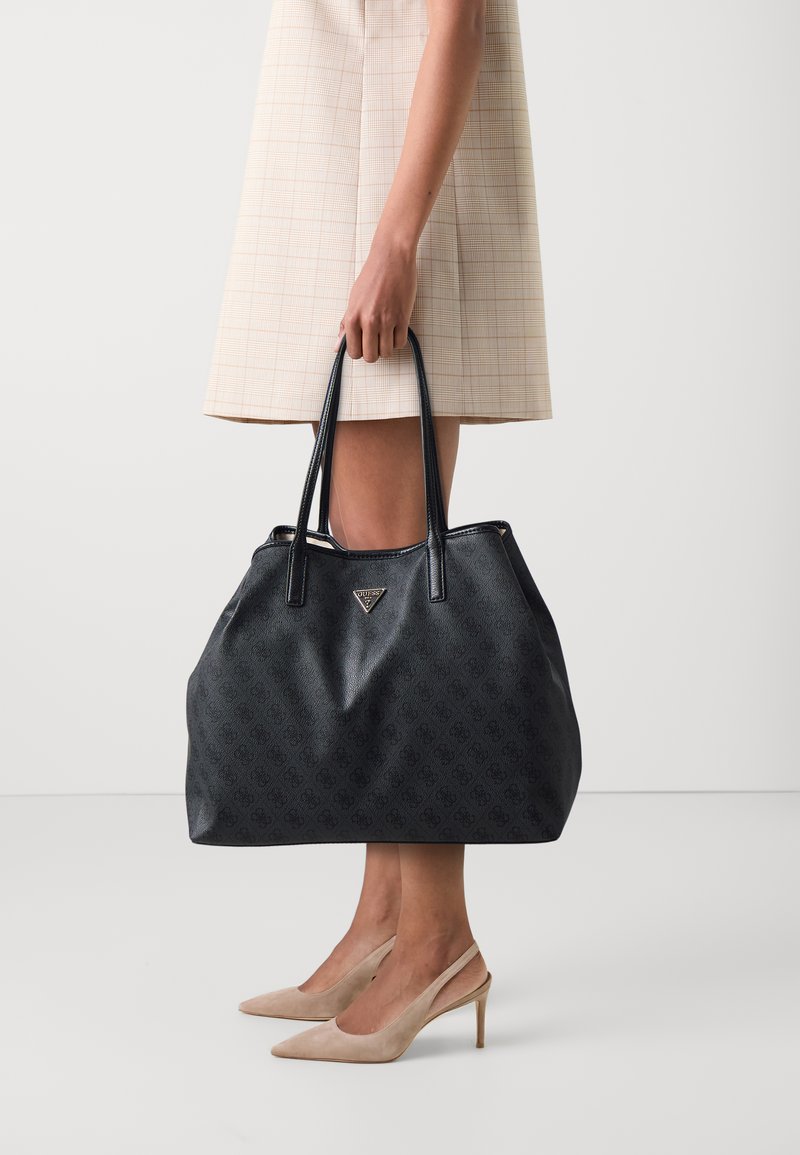 Zwarte leren tote bag met een gestructureerd patroon, dubbele handvatten en een zilveren logo-accent. Heeft een ruime en zachte silhouet.
