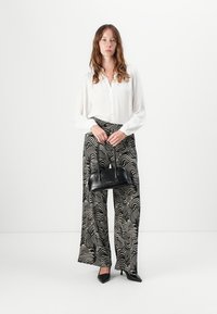 White blouse with button-down front, high-waisted black and white patterned wide-leg trousers, and a small black handbag. Black heels complete the look.