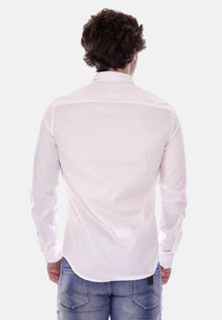 Camicia bianca a maniche lunghe con una texture liscia e orlo curvo. Presenta un colletto classico ed è abbinata a jeans azzurri chiari.