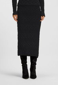 Czarna midi spódnica z lekko fakturowanej tkaniny w geometryczny wzór, zestawiona z czarnymi botasami do kolan. Prosta, dopasowana sylwetka.