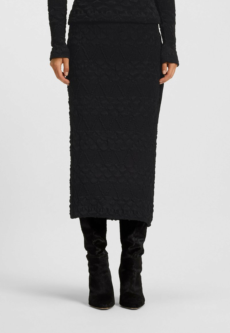 Czarna midi spódnica z lekko fakturowanej tkaniny w geometryczny wzór, zestawiona z czarnymi botasami do kolan. Prosta, dopasowana sylwetka.