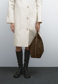 Beige knappad kappa med långa ärmar, svarta knähöga stövlar och en brun läderhandväska med dragkedja och rem.