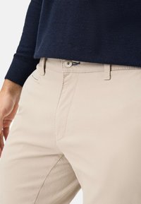 Beige katoenen broeken hebben een slank pasvorm ontwerp, met een knoopsluiting, zijzakken en een gladde textuur. Gestyled met een donkergroen trui.