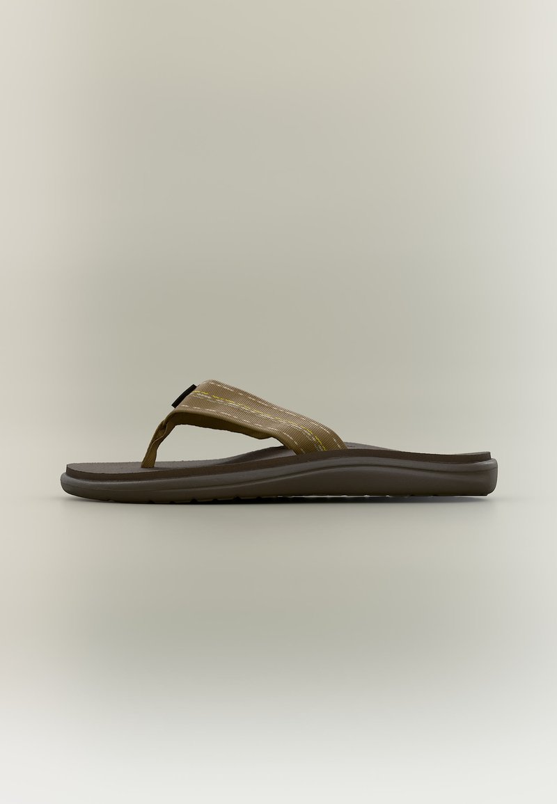 Καφέ σαγιονάρα με υφασμάτινο λουράκι ανάμεσα στα δάχτυλα με κίτρινη ραφή και ελαφρώς σχηματισμένη σκούρα σόλα σε απλό φόντο.