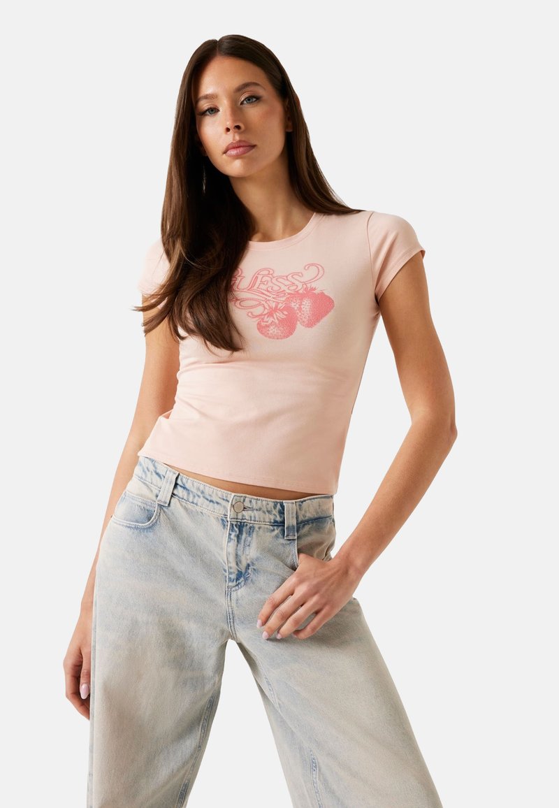 Lichtroze getailleerd T-shirt met korte mouwen en een ronde halslijn, featuring een aardbei-graphic in het rood. G gedragen met lichtblauwe denim jeans.