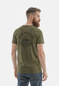 Olivgrünes Baumwoll-T-Shirt mit kurzen Ärmeln, das ein schwarzes geometrisches Bären- und Bergdesign auf dem Rücken zeigt, leichtes Material.