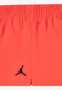Φωτεινά κοραλί σορτς με ελαστική μέση, διακοσμημένα με μαύρο κεντημένο λογότυπο Jordan στη αριστερή πλευρά και μαλακό, ελαφρύ ύφασμα.