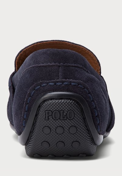 Tumed sinine sametist libisemise jalanõud pehme tekstuuriga, kontrastse pruuni nahkvoodriga ja must kummist tald, millel on ringikujulised haardepinnad ja "Polo" logo.