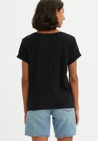 T-shirt noir à manches courtes avec ourlets retroussés, présentant une coupe ample et un tissu léger, associé à un short en denim bleu clair.