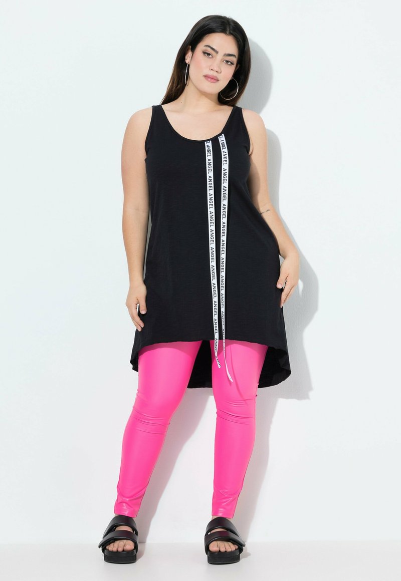 Top nero senza maniche con una striscia bianca con il marchio al centro, abbinato a leggings rosa lucidi e sandali neri con zeppa.