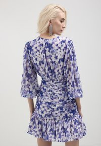 Robe florale dans des nuances de violet et de blanc, avec un corsage ajusté à fronces, un ourlet évasé et des manches bouffantes.
