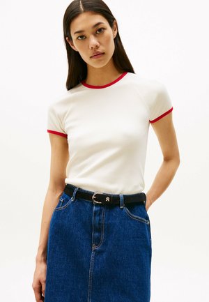 Camiseta blanca de canalé con cuello y mangas rojas, combinada con una falda de mezclilla azul y un cinturón negro. Ambas prendas presentan un diseño ajustado.