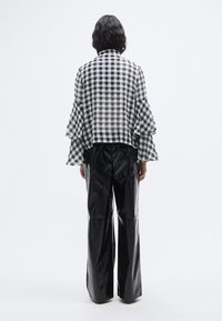 Μπλούζα σε ασπρόμαυρο καρό gingham με βολάν στα μανίκια, συνδυασμένη με μαύρο, γυαλιστερό παντελόνι φαρδιάς γραμμής και ψηλόμεσο. Το υφή του υφάσματος δημιουργεί αντίθεση με τις σιλουέτες.