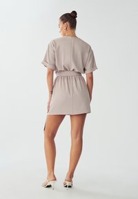 Lichtbeige kort jurkje met een relaxte pasvorm, opgerolde mouwen, elastische taille en een zijsplit, gemaakt van een soepele stof. Eenvoudig ontwerp aan de achterkant.