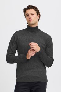 Tmavosivý rolákový sveter zo  mäkkej pleteniny s dlhými rukávmi a rebrovaným lemom a manžetami, nosený s čiernymi nohavicami.