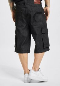 Zwarte denim cargo shorts met een knielange snit, zijzakken en gestikte details. Draagt met witte sneakers. Leren patch op de tailleband.