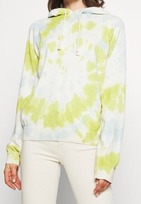 Huvtröja i mjukt tyg med ett tie-dye-mönster i grönt och blått på en vit botten. Ribbad mudd och nederkant.