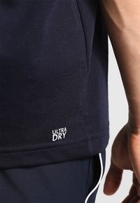 Camiseta de algodón azul marino con etiqueta ULTRA DRY. Textura suave, mangas cortas y un corte relajado, con un dobladillo recto y costuras mínimas.