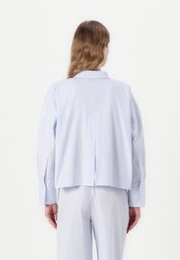 Camisa de botão listrada em azul e branco com um corte descontraído, mangas dobradas e detalhe de pregas nas costas. Tecido suave, com uma marcação mínima na parte de trás.
