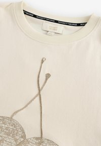 Kremna sweatshirt z nežnim srebrnim vezenjem abstraktnih oblik in črt. Žeprižana ovratnica za teksturo, oznaka vidna znotraj.
