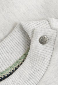 Gestreepte witte trui kraag met een metalen knoop met een klaverthema en een groene en zwarte geprinte rand aan de binnenkant.