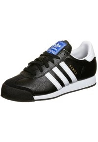 Černobílé sportovní boty s texturovaným koženým svrškem, třemi bílými pruhy, černými tkaničkami, modrým logem na jazyku a gumovou podrážkou.