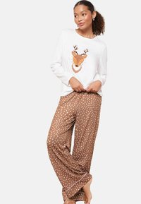 Bílý top s dlouhým rukávem a grafikou jelena. Hnědé kalhoty s puntíky s hladkou texturou a širokými nohavicemi. Jednoduchý design a měkká tkanina.