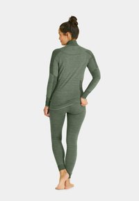 Woman in gray-green seamless long-sleeve top and leggings, standing barefoot with back facing, hair tied in a bun.