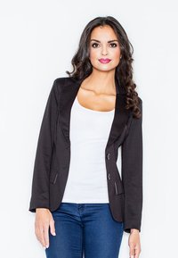 Zwarte blazer met satijnen revers en twee knopen, met een getailleerde pasvorm en zakken, gedragen over een witte top en blauwe jeans.
