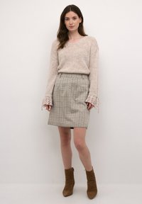 Beige strikket trøje med løse ærmer, parret med en grå ternet blyantskørter og brune ankelstøvler. Teksturerede materialer og subtile designdetaljer.