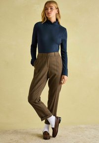 Námornícky pruhovaný top s dlhým rukávom a volánovým golierikom, doplnený hnedými kockovanými nohavicami s vysokým pásom. Obuvou sú hnedé mokasíny a biele ponožky.