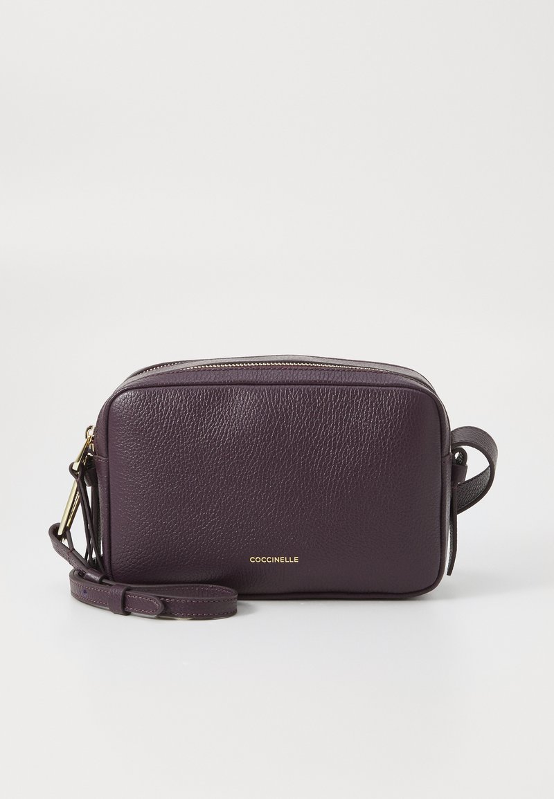 Fioletowa skórzana torebka typu crossbody z teksturowanym wykończeniem, złotym okuciem, zapięciem na zamek i regulowanym paskiem; na przodzie posiada logo marki.