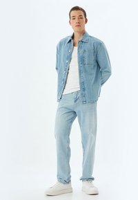 Ljusblå denimskjorta med bröstficka, matchad med ljusblå jeans och vita sneakers. Slät textur, klassisk passform.