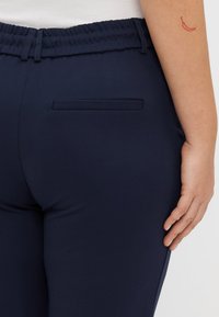 Marineblaue Hose aus glattem, dehnbarem Stoff. Mit einem gerafften Bund und einer einzelnen Gesäßtasche auf der rechten Seite.