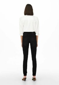 Svarta skinny jeans med bakfickor, hög midja och subtila sömnadsdetaljer; tillsammans med en vit skjorta med knappar och puffärmar.