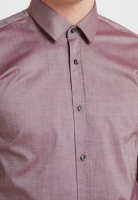 Camisa de manga corta color lila claro con acabado texturizado, presenta un cuello puntiagudo y botones oscuros en la parte delantera.