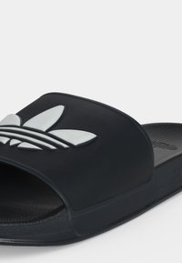 Black slide sandal with wide strap featuring a raised white Adidas trefoil logo on a plain background.