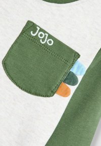 Vihreä taskupaita, jossa on vaaleanharmaa pinta. Taskussa vihreitä, sinisiä ja oransseja yksityiskohtia. Pehmeä puuvillamateriaali ja pyöreä kaula-aukko.