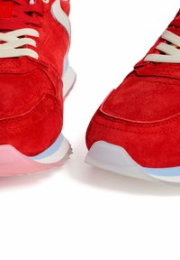 Zapatillas de ante rojas con cordones blancos, acentos azules y rosas en la suela, con un acabado texturizado y elementos de diseño curvados.