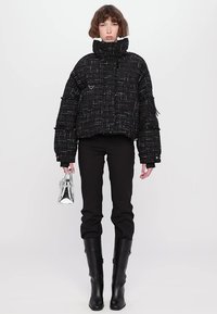 Melnas tweed stila īsās pūkainās jakas ar augstu apkakli, teksturētu audumu un atstarojošiem akcentiem. Apvienota ar melnām biksēm un augstiem zābakiem līdz ceļiem.