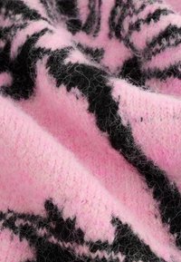 Stickad tröja i rosa med ett svart abstrakt mönster, som visar en mjuk, texturerad yta med synliga fibrer.