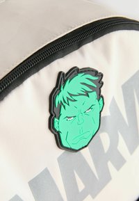 Valkoinen kangaskassi, jossa on suuri vihreä Hulk-naamapatch, musta vetoketju ja harmaa "MARVEL"-teksti.