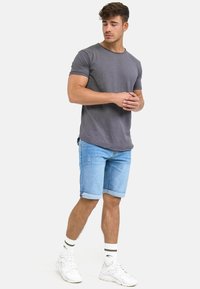 Szary t-shirt z okrągłym dekoltem zestawiony z jasnoniebieskimi szortami dżinsowymi, podwiniętymi na końcach, oraz białymi trampkami z czarnymi paskami na skarpetkach.