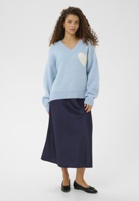 Pull tricoté bleu clair avec un motif cœur blanc, associé à une jupe midi en satin bleu marine et des ballerines noires. Texture douce et coupe décontractée.