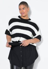 Pull en tricot rayé noir et blanc avec des manches courtes et un col rond, associé à une chemise noire à boutons et un legging en simili-cuir.