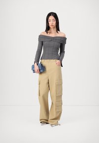 Gray ribbed off-shoulder top and beige cargo pants with multiple pockets. The model holds a blue handbag and wears silver shoes.