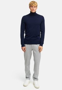 Marineblauer Rollkragenpullover kombiniert mit hellgrauen Jogginghosen und weißen Turnschuhen. Der Pullover hat ein enganliegendes Design und eine weiche Textur.