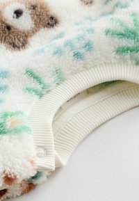 Sluppy hvid sweatshirt med bjørnemotiv, med grønne og blå accenter, ribbede hvide manchetter og en lille trykknapdetalje.