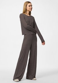 Ribade loungewear komplekt tumepruuni ja valgega, mis sisaldab kastikujulist pika varrukaga toppi ja laiad püksid, millel on pehme tekstuur.